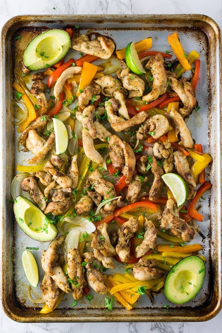 Chicken, bells peppers, and onion fajitas on a sheet pan with limes and avocado