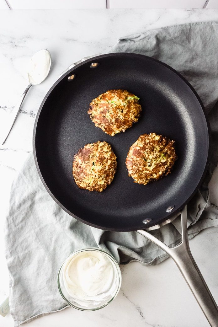 low-carb zucchini fritters in a frying pan with sour cream